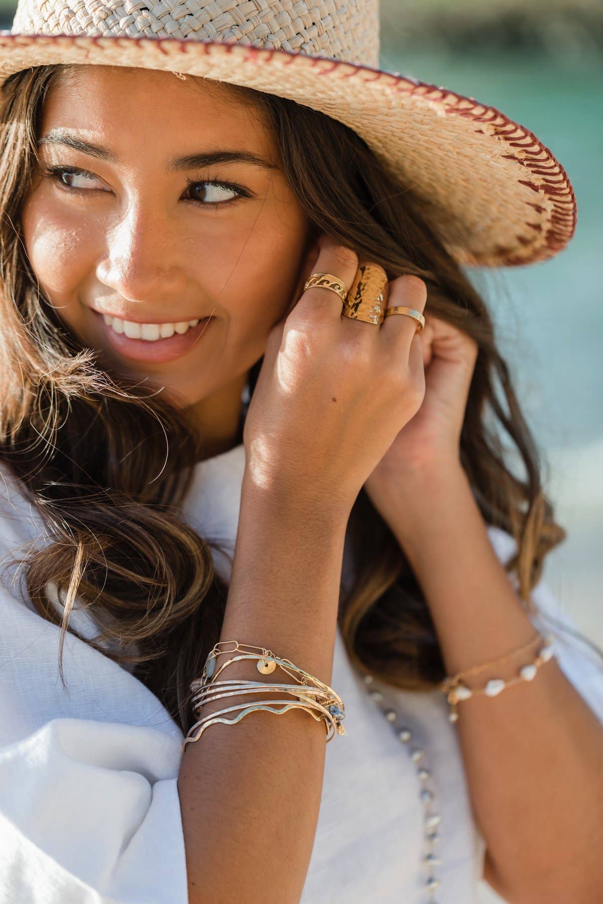 Woman wearing a straw hat and gold jewelry by a body of water