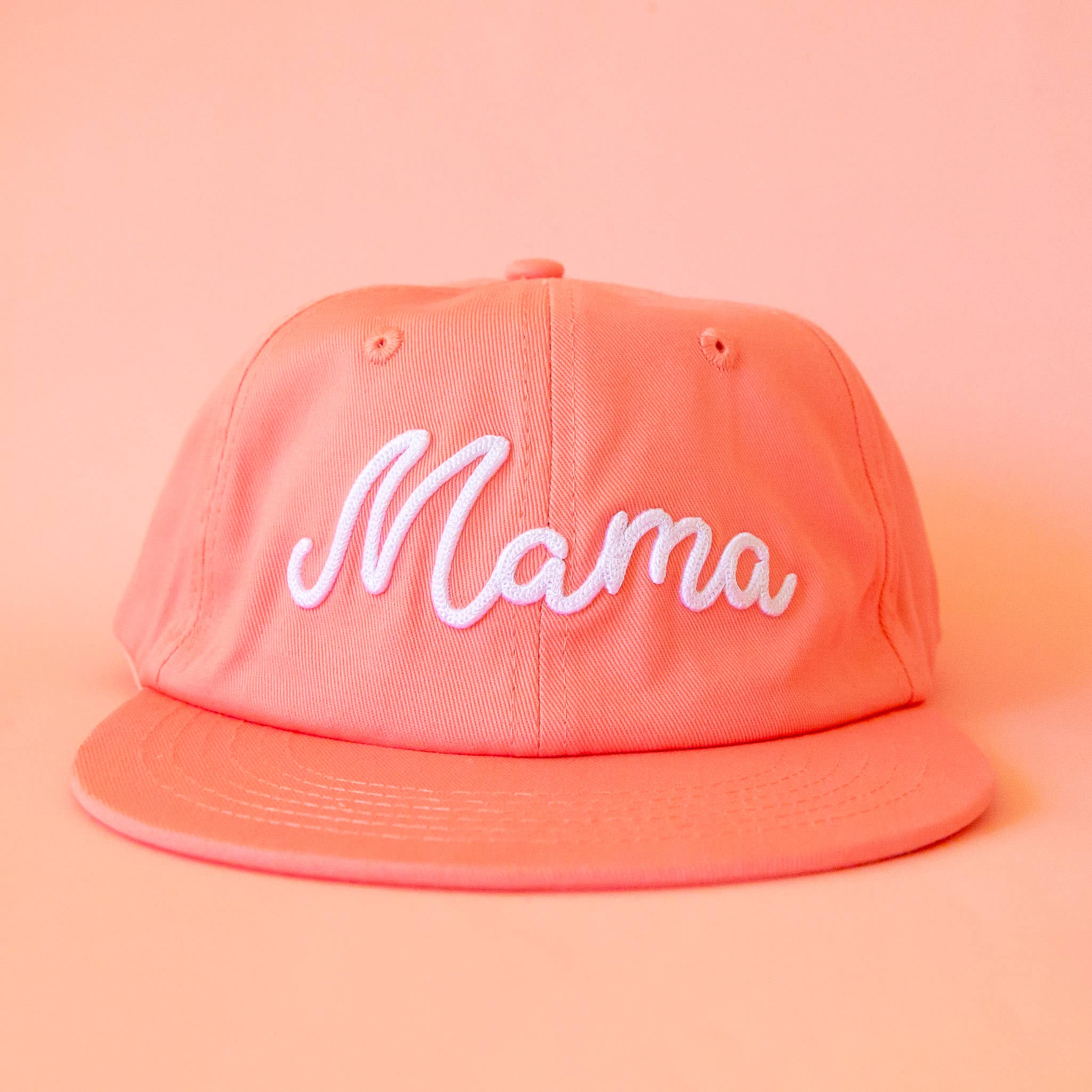 A peachy pink flat brim hat with the word 'Mama' embroidered in white on the front.